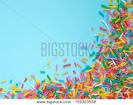 Border frame of colorful sprinkles on blue background with copyspace. Top view or flat lay