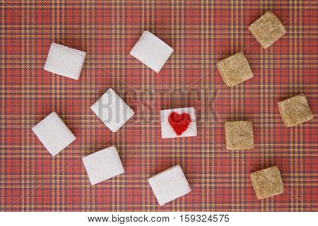 Sugar cubes with a red heart on one of them as background. Top view. Diet unhealty sweet addiction concept