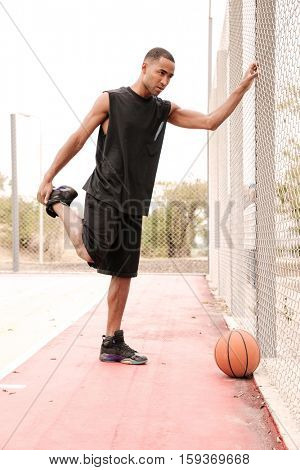 Photo of young african basketball player making sport exercises. Shooting at basket outdoor.