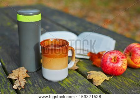 Hot Tea, Mug, Apples And Book On A Picnic Table On A Fall Day
