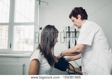 General practicioner measuring her patient's heart pressure and smiling to patient. Interacting and taking care of patient. Taking care of your health. Disease prevention.