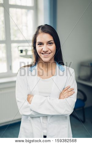 Portrait of a confident young female doctor standing in her office, smiling at camera. Health care and prevention concept. Friendly and approachable medical care from practicioner.