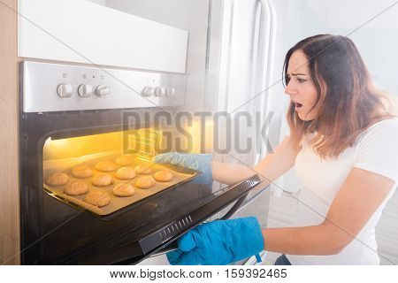 Young Shocked Woman Looking At Burnt Cookies From Oven