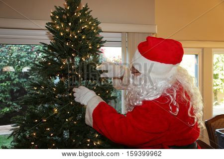 Santa Claus prepares a Christmas Tree with Lights and ornaments for Christmas at a persons house. Santa Loves xmas. x-masTree.   Santa Claus setting.