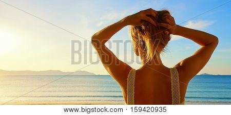 A back side view on a wonderful young woman watching to sea and raising her hands on sunrise.Panoramic view