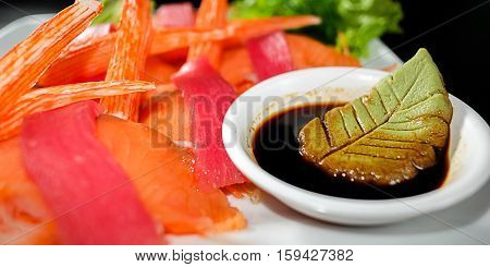 Tuna sashimi and crabstick with soy sauce on black background