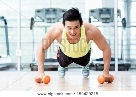 Frontal view of male bodybuilder doing pushups while holding dumbbells in his hands