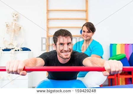 Young man working out in physical therapy on swiss ball with gymnastic stick