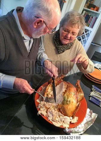 Senior Adult Couple Cutting the Holiday Turkey Together In The Kitchen.
