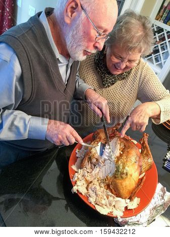 Senior Adult Couple Cutting the Holiday Turkey Together In The Kitchen.