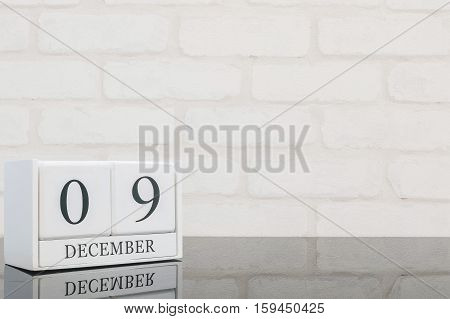 Closeup white wooden calendar with black 9 december word on black glass table and white brick wall textured background with copy space selective focus at the calendar