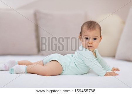Baby girl on white bed. Cute baby girl lying on her tummy