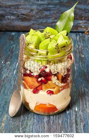 Garnet apple persimmon pear kiwi yogurt oatmeal in a jar Fruit salad black background