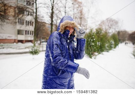 Woman turns aside from the snowballs flying to her. Someone fires at her snowballs. She pulls a hood over the face and cheerfully laughs. All ground is completely covered with fluffy snow.