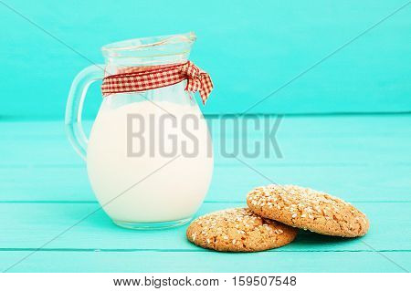 Jug of milk with plaid ribbon and oat cookies on blue wooden kitchen. Copy space