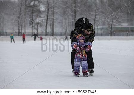 Saint-Petersburg Russia - December 2 2016: Urban outdoor ice rink in the park. Father teaching his child to skate.