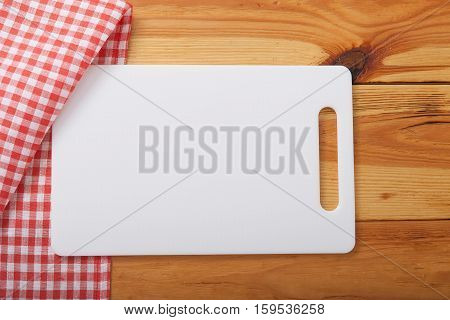 Empty white cutting board over towel on wooden kitchen table. Top view