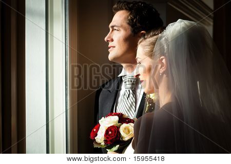 Noivos de pé na janela no casamento deles e olhando para fora