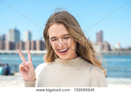 Beautiful girl with funny face expression showing tonque and victory fingers sign outdoors