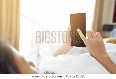 Concentrated young Asian girl looking at her smartphone lying on the bed in bedroom. Technology and internet concept. Copy space. Preteen or school age girl using smart phone on the bed in the morning
