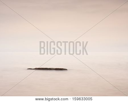 Romantic morning at sea. Big boulders sticking out from smooth wavy sea. Pink horizon with first hot sun rays. Vintage Style effect