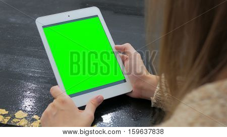 Woman looking at vertical tablet computer with green screen. Close up shot of woman's hands with pad