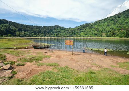 Beautiful landscape of the Laguna Verde with a boat in Apaneca Ruta de Las Flores itinerary El Salvador Central America. The text in Spanish says: don't fish with harpoon don't swim don't throw plates nor stones into the water don't wash dogs