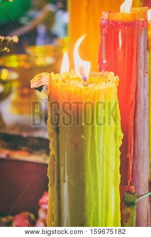 Burning red and yellow beautiful old textured candles with defocussed background of buddhist temple Thailand. Mood of sacrament and revelation.