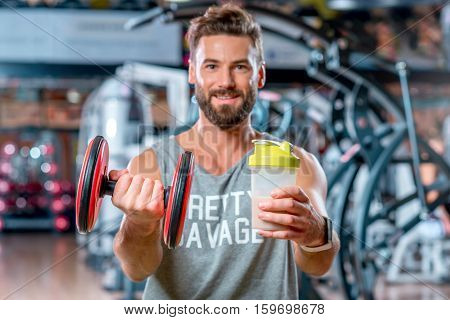 Muscular man holding dumbbell and a bottel with sports nutrition in the gym
