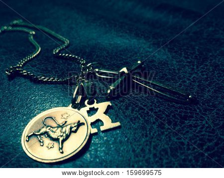 A necklace with three pendants: a letter k a cross and the bull zodiac sign