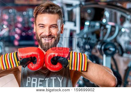 Portrait of muscular smiling boxer with red boxing gloves in the gym
