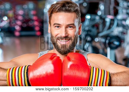 Close-up portrait of muscular smiling boxer with red boxing gloves in the gym
