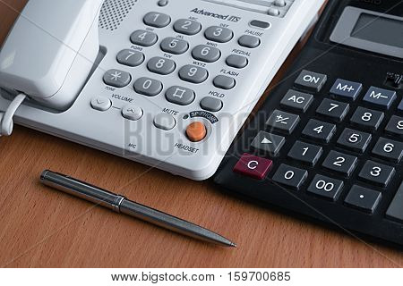 telephone calculator and metal ballpoint pen lying on a light wooden table in the office at work preparing for the working day and making cold calls to clients