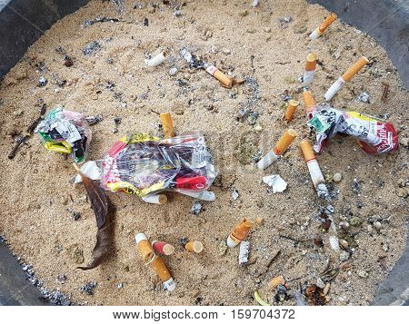 CHIANG RAI THAILAND - NOVEMBER 25: Used cigarette butt in dirty ash tray with sand and crumpled cigarette case on November 25 2016 in Chiang rai Thailand