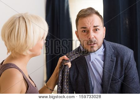 Man under pressure of his angry wife. Blond lady wife keeping her husband's tie and screaming at him. Family concept. Quarrel concept.