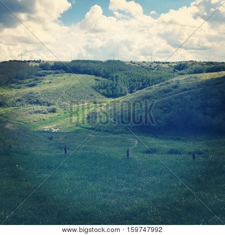 Field landscape in summer.  Lush dark green valley and hills with old wire fence and posts, bright lush green trees and grass. Bright blue sky, dark and white clouds background.