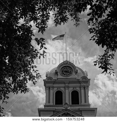 The American Flag flies prondly on top of the historic Crook County Courthouse in Prineville in Central Oregon on a summer afternoon. The scene is framed with trees.