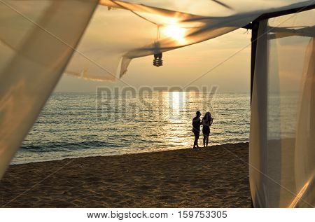 Silhouette of happy Romantic couple boy and girl enjoy beautiful sunset walk on beach with white transparent curtain foreground. Travel vacation new generation Lifestyle Concept. Happy Valentine's day