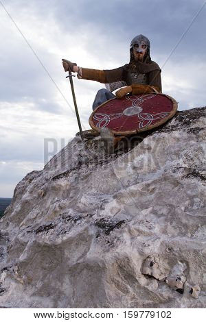 Knight sitting on a rock with a sword against blue cloudy sky