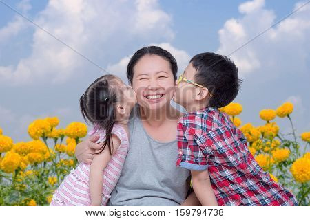 Asian boy and girl kissing their mother in park