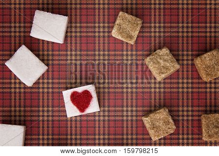 Sugar cubes with a red heart on one of them as background. Top view. Diet unhealty sweet addiction concept