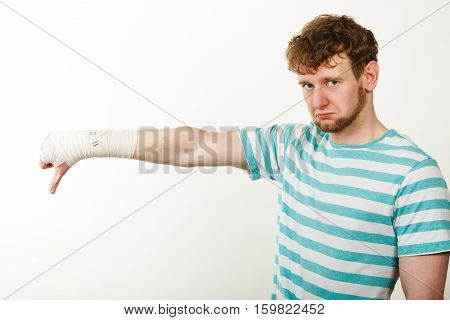 Bad news and information. Medicine aspects. Sad unhappy male with bandaged hand showing thumb down sign symbol.