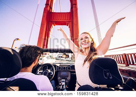 Happy couple driving on a convertible car - Road trip to San Francisco woman with raised arms greeting Golden Gate Bridge