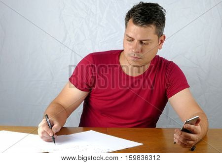 Young Man Writing On A Paper And Holds Smart Phone In His Hand