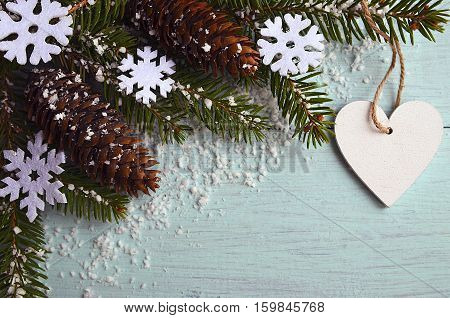 Christmas decoration.Decorative snowflakes,fir cones,heart and snowy fir tree branch on light blue background with copyspace.Winter holidays,Merry Christmas or Happy New Year concept.Selective focus.
