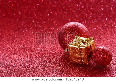 Red christmas glitter background with two ball golden wrapped gift box selective focus