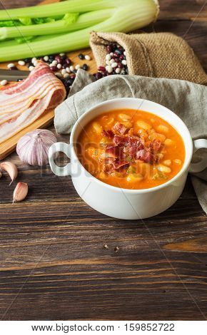 Homemade bean soup in white bowl on rustic wooden background with ingredients.