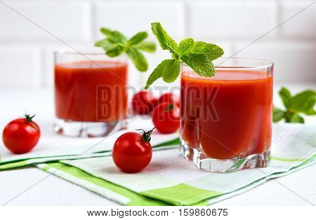 Tomato juice in a glass with a cherry and mint on a light background