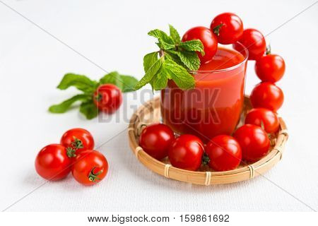 Tomato juice in a glass with a cherry and mint on a light background