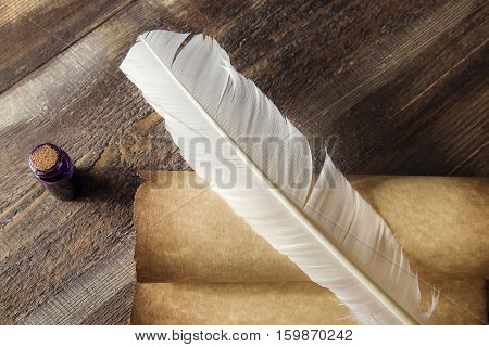 Writing concept. Closeup of scroll and quill near ink-pot on wooden table.
